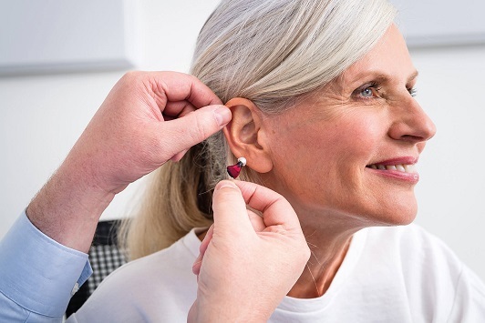 Ältere Frau bekommt von einem Hörgeräteakustiker ein modernes Hörgerät eingesetzt.